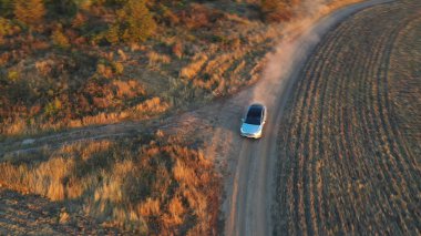 Tozlu yoldan hızla geçen elektrikli arabanın havadan görüntüsü. Kırsal yol boyunca giden elektrik yükündeki ekoloji dostu otomobil. Özgürlük kavramı ya da modern teknoloji. Yavaş çekim.