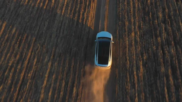 Aerial view of electrical car driving through country road. Drone following to modern vehicle moving fast along ground path. Ecology friendly car riding on electric charge along motorway