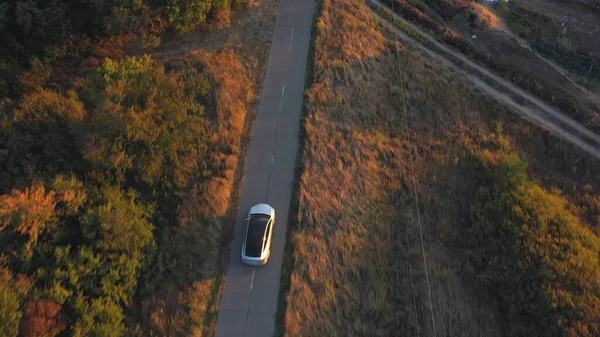 Aerial shot of electrical car driving through country road at summer evening. Modern vehicle passing rural highway. Ecology friendly car riding on electric charge along motorway. Top view Slow motion.