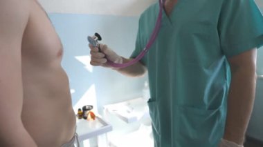Doktor steteskoplu erkek hastada COVID-19 semptomları arıyor. Doktor genç adamın ciğerlerini dinler. Doktor, hastanedeki adamın göğsünü kontrol etti. Koronavirüs salgınından korunma kavramı