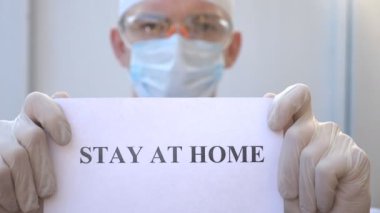 Sıhhiyeci kendini izole etmeye meyilli bir poster gösteriyor. Erkek doktor, Coronavirus salgını sırasında evde duran bir resim tutuyor. COVID-19 salgınından korunma kavramı