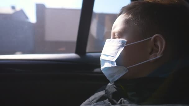 Niño pequeño con mascarilla médica viajando en coche y mirando por la ventana. El niño triste usa una máscara protectora del virus durante el viaje. Concepto de salud y seguridad de la pandemia de coronavirus — Vídeos de Stock