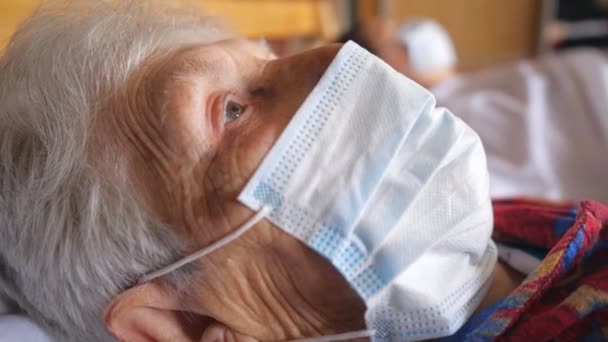 Cara cercana de la anciana con máscara protectora del virus. Enfermera con mascarilla médica acostada en la cama en el hospital. Concepto de vida de salud y seguridad a partir de coronavirus o pandemia. Dolly disparó — Vídeo de stock