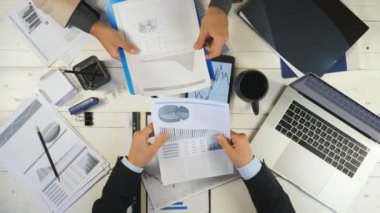 Grafikleri kontrol eden ve ofiste mali raporları tartışan iki genç iş adamının üst düzey erkek eli. Başarılı iş arkadaşları masada oturuyor ve yeni bir iş projesi geliştiriyor.
