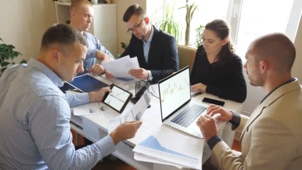 Les gens d'affaires discutent des graphiques et des tableaux de revenu lors d'une réunion d'équipe dans un bureau moderne. Jeunes collègues assis à la table et analysant les rapports financiers. Travailleurs examinant les documents au bureau — Video