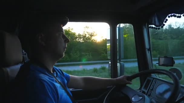 Profil du conducteur de camion circulant dans la campagne à l'heure du coucher du soleil. Homme en chapeau contrôlant son camion attentif regarder la route. Vue de l'intérieur de la cabine du camion. Concept de transport de fret. Ralentir mo Fermer — Video