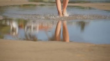 Dişi bacakları alçak görünüm deniz kıyısının yakınındaki büyük su birikintisine basar. Çıplak ayaklı genç bir kadın kıyıya yakın boş tropikal plajda yürüyor. Yaz tatili ya da tatil konsepti. Yavaş çekim