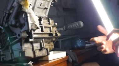 Tamirci garajda veya atölyede otomobil motoru tamir ediyor. Tamirci otomatiğe geçti. Adam işi için karanlıkta parlak el feneri kullanıyor. Yavaş çekim. Yakın çekim.