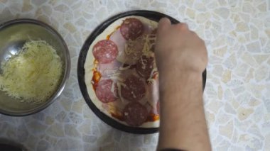 Aşçı erkek eli rendelenmiş peyniri hamur işine koyuyor. Mutfakta metal malzemelerle birlikte. Şef mutfakta ahşap yüzeyde pepperonili pizza yapıyor. Yemek hazırlama konsepti. Üst Görünüm Yavaş çekim