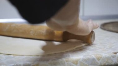 Mutfaktaki ahşap bir yüzeye pizza hamuru döken şefin genç elleri. Lokantadaki mutfak masasında merdane kullanarak hamur işi yapan bir aşçının erkek kolları. Yemek pişirme konsepti. Kapat.