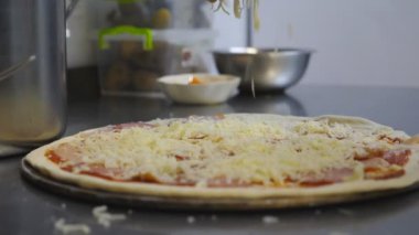 Aşçının erkek eli hamur işine rendelenmiş peynir atıyor ve mutfakta metal malzemeler var. Şef, mutfaktaki ahşap yüzey üzerinde pepperoni pizzası hazırlıyor. Yemek pişirme kavramı. Dolly vurdu.