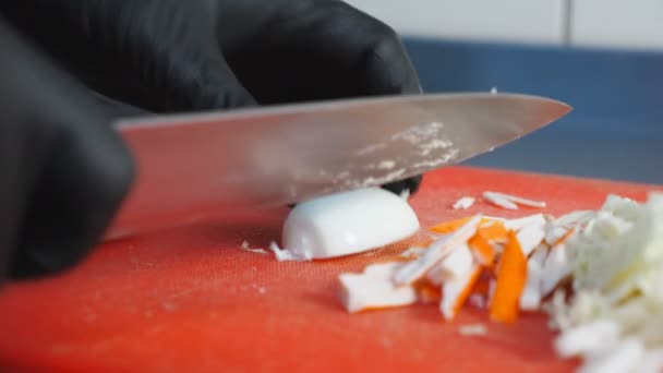Tangan laki-laki memasak dalam sarung tangan memotong setengah telur rebus dan mengirisnya di papan pemotong plastik menggunakan pisau. Proses pembuatan salad sayuran yang sehat. Konsep makanan memasak. Gerakan lambat — Stok Video