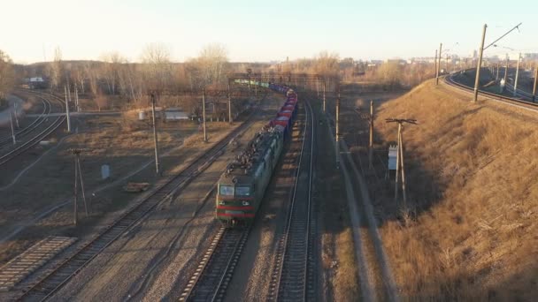 Воздушный кадр поезда, движущегося по железной дороге и перевозящего промышленные товары. Беспилотник пролетает над локомотивом с грузовыми вагонами, проходящими по сельской местности. Концепция транспортировки или доставки грузов. Вид сверху — стоковое видео