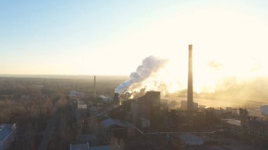 Endüstri bölgesinin hava görüntüleri borulardan atmosfere duman yayıyor. İHA fabrikanın üzerinde uçuyor ya da bitki zehirli buharı arka planda güneş ışığıyla havaya yayıyor. Doğa kirliliği sorunu. Üst görünüm.