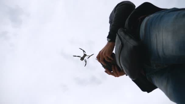 Χαμηλή θέαση σε αγνώριστο άνθρωπο που ελέγχει drone μέσω τηλεχειρισμού. Quadcopter χειριστή tacking εναέρια εικόνες ή κινηματογράφηση βίντεο από γραφικό περιβάλλον. Σύγχρονη τεχνολογία έννοια. Αργή κίνηση — Αρχείο Βίντεο