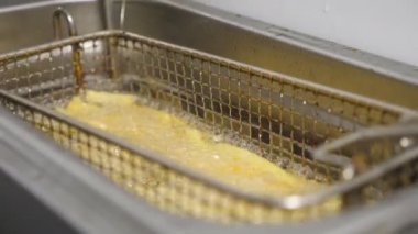 Erkek aşçının, kızgın yağda kızartılmış patates kızartmasıyla ızgarayı sallamasına yakın çekim. Şef patatesle kafesi fritözün içine indiriyor. Mutfakta fast food yapma süreci. Yavaş çekim