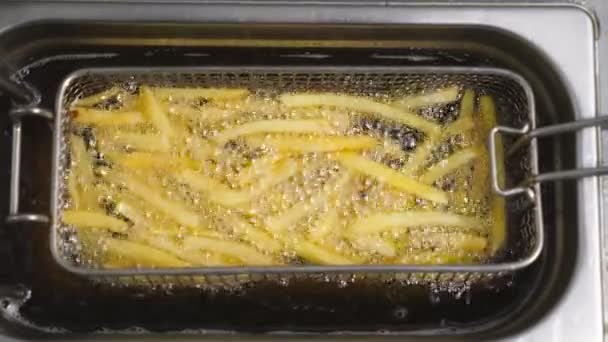 Tasty french fries is cooking into deep fryer at kitchen. Crispy potatoes is frying in hot boiling oil at cuisine. Process of making fast food. Concept of preparing food. Top view Slow motion — Stock Video