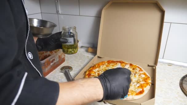Männliche Hand des Kochs im Handschuh legt Knoblauchöl auf fertige vier Käse-Pizza-Kruste mit einer Silikonbürste. Leckeres Gebackenes im Karton in der Küchenpizzeria. Konzept der Essenszubereitung. Nahaufnahme — Stockvideo
