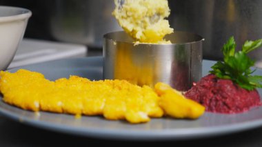 Aşçının erkek elini kapat. Patates püresini kaşıkla mutfaktaki demir kalıba koy. Şef ekmek arası tavuk filetosu ile püre servis ediyor. Yemek hazırlama kavramı. Yavaş çekim.