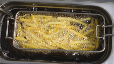 Lezzetli patates kızartmaları mutfakta fritöze dönüşüyor. Kızarmış patatesler mutfakta kızgın yağda kızartılıyor. Fast food yapma süreci. Yemek hazırlama kavramı. Üst Görünüm Yavaş Çekim.