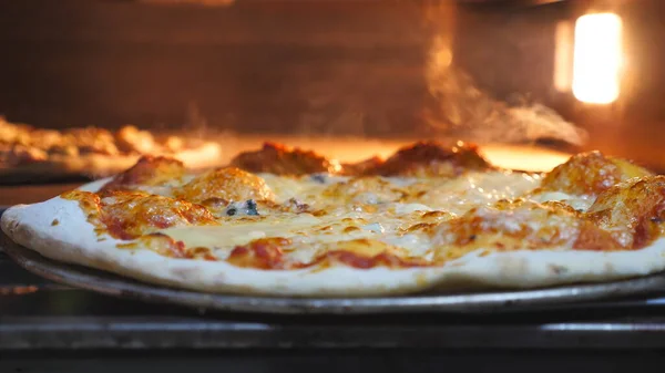 Male cook taking out four cheese pizza from electric oven using a shovel and putting it table at cuisine. Young cook baked delicious dish at kitchen restaurant. Concept of preparing food. Slow motion.