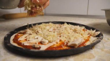 Aşçının eli rendelenmiş peyniri hamur işine koyuyor ve malzemeler mutfakta metal formda. Aşçı mutfağın ahşap yüzeyinde İtalyan pizzası yapıyor. Yemek pişirme kavramı. Dolly çekim ağır çekim