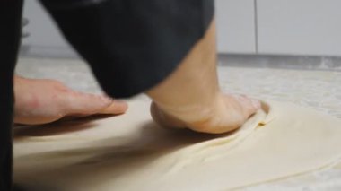 Aşçının erkek kollarını kapayarak mutfaktaki ahşap bir yüzeyde hamur işi oluşturuyorlar. Restorandaki mutfak masasında pizza için un hamuru şekillendiren şefin elleri. Yemek hazırlama kavramı. Yavaş çekim