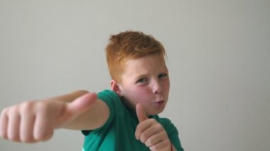 Mutlu kızıl saçlı çilli çocuğun portresi. Sevimli yakışıklı bebek başarıyı alkışlıyor ve baş parmağını kaldırıyor. Yüzünde neşe ifadesi olan erkek çocuğun duygularını kapat. Yavaş çekim