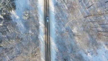 Karla kaplı buzlu yolda uçan beyaz arabanın görüntüsü. SUV kış günü ormandaki boş kırsal yolda gidiyor. Otomotiv üzerinde uçmak manzaralı bir yolda ilerlemek. Üst görünüm