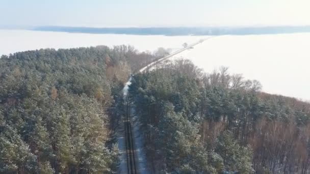 Zdjęcie białego SUV-a jadącego pokrytą śniegiem leśną drogą. Jazda samochodem po lodowatych lasach zimą. Auto przejeżdża przez piękną przyrodę. Pojęcie podróży i aktywnych weekendów. Powyżej widoku — Wideo stockowe