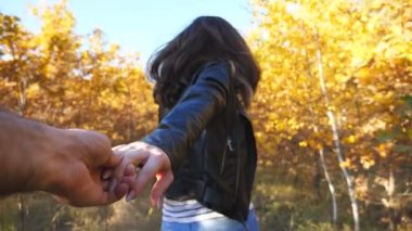 Genç kadın erkek elini tutuyor ve bahçede patika boyunca koşuyor. Beni takip edin. Mutlu kız, erkek arkadaşını meşe ağaçlarının arasından çekiyor. Arka planda güzel bir doğa. Sevgi kavramı. POV