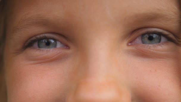 Luk af blå øjne glad lille pige blinker og ser ind i kameraet med et lykkeligt syn. Portræt af søde ansigt af unge smilende barn ser med positive følelser. Forside – Stock-video