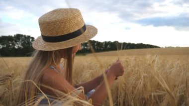 Hasır şapkalı küçük çocuk mısır gevreğini elinde tutarken buğday tarlasında oturuyor. Mısır gevreği tarlasında arpa sapıyla oynayan uzun sarı saçlı güzel bir kız. Yavaş çekim