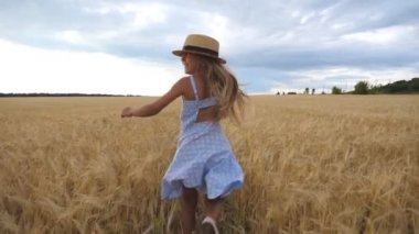 Buğday tarlasında koşuşturan uzun sarı saçlı güzel kız kameraya dönüp gülümsüyor. Hasır şapkalı şirin çocuk bulutlu bir günde arpa çayırında koşuyor. Yavaşça kapat.