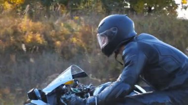 Otoyolda motosiklet süren kasklı bir adam. Arka planda güneş ışığı var. Sonbahar kır yolunda motosikletini kullanan bir motosikletli. Yavaş çekim kenar görünümü Kapat