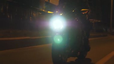 Geceleri farları açık modern motosiklet süren bir adam. Motosikletli biri karanlık şehir caddesinde motosikletiyle yarışıyor. Yolculuk sırasında bisiklet süren adam. Özgürlük ve macera kavramı. Ön görünüm