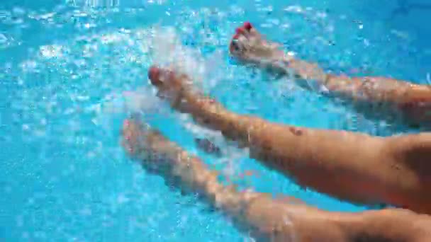 Jonge vrouwen die op de rand van het bassin zitten en hun voeten bungelen in aqua. Twee meisjes spelen hun benen in helder water van het zwembad. Dames genieten van vakantie in het resort. Begrip zomervakantie. Langzame beweging — Stockvideo
