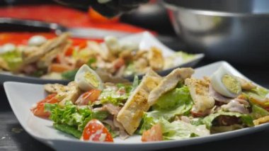 Erkek eli kaynamış bıldırcın yumurtalarını Sezar salatasının üzerine beyaz tabakta koyuyor. Eldiven giymiş aşçı kolu servis edilmek üzere lezzetli yemekler hazırlıyor. Yemek pişirme kavramı. Ağır çekim.