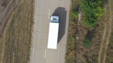 Beyaz kargo karavanı olan bir kamyonun boş yolda giderken ve malları taşırken hava görüntüsü. Bir teslimat kamyonu taşra otobanından geçiyor. Lojistik konsept. Üst görünüm