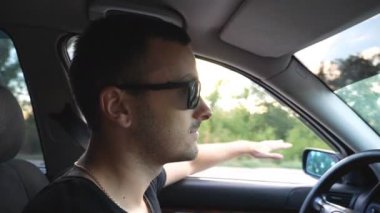 Kırsalda araba kullanan güneş gözlüklü yakışıklı bir adamın profili. Elleri rüzgarda hareket eden ve yolculuğun tadını çıkaran tasasız genç bir adam. Seyahat konsepti. Yan görünüm Yavaş çekim