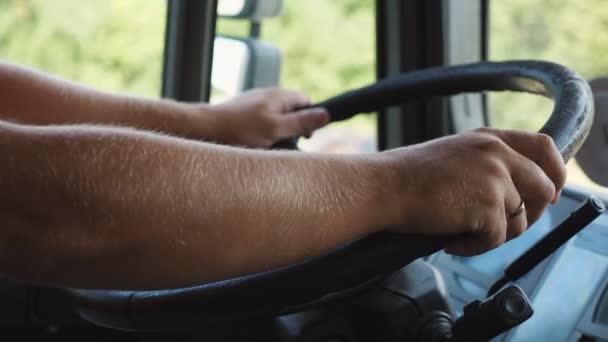 Мужские руки водителя грузовика держат большое руль во время вождения грузовика в солнечный день. Дальнобойщик едет к месту назначения по проселочной дороге. Концепция логистики и транспорта. Закройте Долли. — стоковое видео