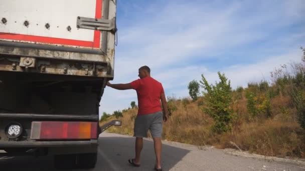 Motorista do sexo masculino caminhando ao longo da estrada perto de seu caminhão estacionado no campo. O camionista está pronto para continuar a viagem. Bela paisagem no fundo. Baixa visão Movimento lento — Vídeo de Stock