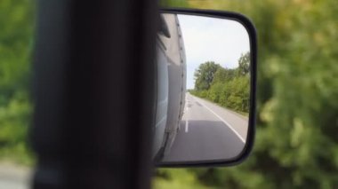 Arka planda boş yolu olan kamyonun yan aynasına bak. Güneşli bir yaz gününde kırsaldan geçen bir kamyon. Lojistik ve ulaşım konsepti. Yavaşça kapat.