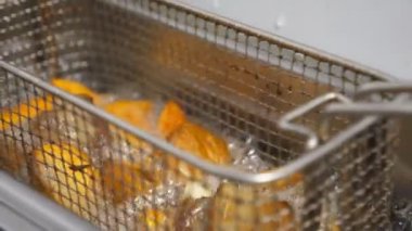 Erkek aşçı patates dilimleri ve kızgın yağda et ile ızgarayı sallıyor. Şef patates köyü parçalarıyla kafesi fritözün içine indiriyor. Yemek hazırlama kavramı. Kapat.