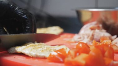 Aşçının erkek ellerini eldivenle kapayın. Mutfakta bıçakla kızarmış tavuk filetosunu plastik kesme tahtasıyla dilimleyin. Sezar salatası hazırlama süreci. Yemek pişirme kavramı. Yavaş çekim