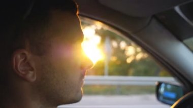 Gün batımında kırsalda araba süren yakışıklı bir adamın profili. Kendine güvenen genç adam otomobili kontrol ederken yola dikkatlice bakıyor. Seyahat konsepti. Yan Görünüm Yavaş çekim Kapat
