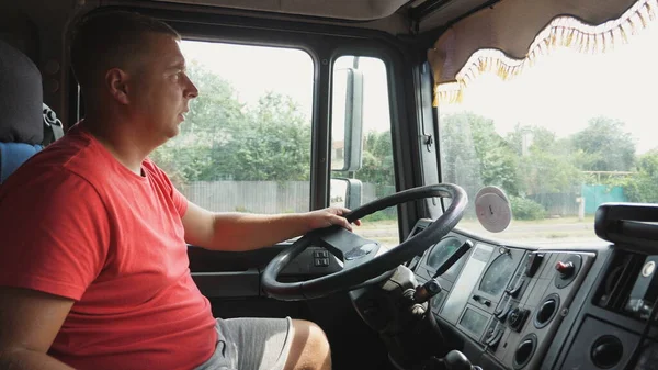 Lorry driver holds hand on a steering wheel and controls car riding to destination. Man operating the truck through countryside. Trucker driving at country road. Logistics and transportation concept.