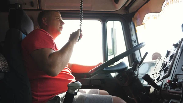 Lorry driver riding through countryside and talking on radio communication. Trucker speaks on walkie-talkie while driving a car on country road. Logistics and transportation concept. Slow motion.