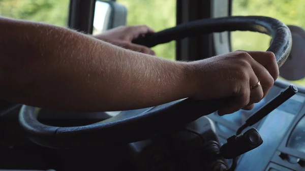 Male hands of lorry driver holds a big steering wheel while driving a truck at summer day. Trucker riding to destination at country road. Concept of logistics and transportation. Close up Slow mo.