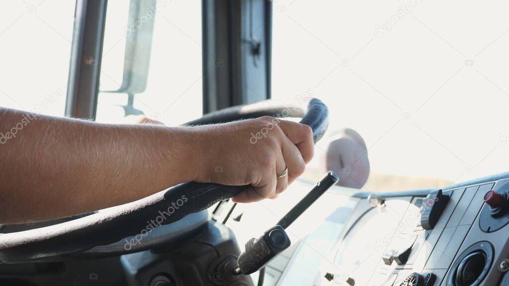 Lorry driver operating the truck through countryside. Trucker holds hands on a steering wheel and controls a car riding to destination. Man driving at country road. Logistics concept. Dolly shot.